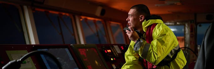 ship crew performing daily duties with VHF radio, binoculars, logbook, standing nearby to ECDIS shutterstock_1471641632