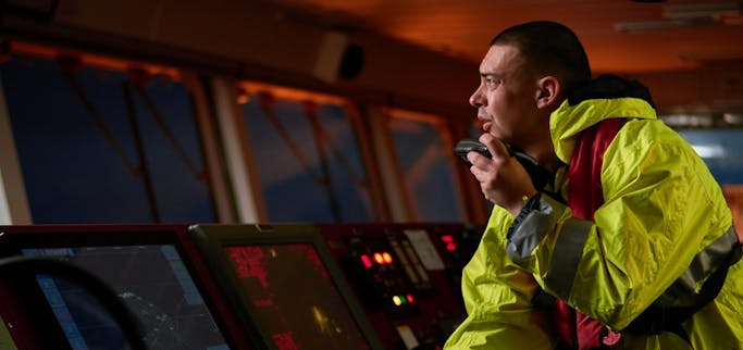 ship crew performing daily duties with VHF radio, binoculars, logbook, standing nearby to ECDIS shutterstock_1471641632